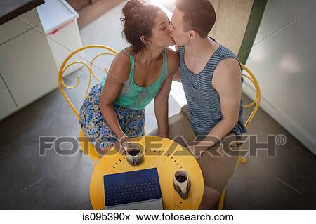 Stock Photo - High angle view of romantic young couple kissing at kitchen table. Fotosearch