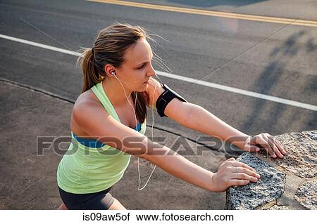 Stock Image - High angle view of woman wearing activity tracker stretching against concrete block. Fotosearch
