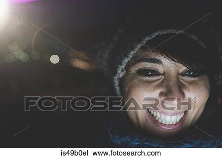 Stock Image - Illuminated close up of happy woman wearing knit hat at night. Fotosearch