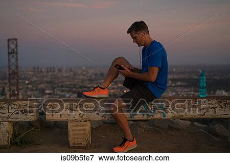 Stock Photo - Jogger sitting on bench looking at smartphone, Runyon Canyon, Los Angeles, California, USA. Fotosearch