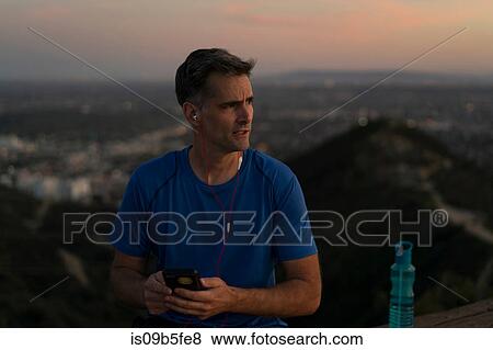 Jogger wearing earphones holding smartphone, Runyon Canyon, Los Angeles, California, USA View Large Photo Image Stock Photo - Jogger wearing earphones holding smartphone, Runyon Canyon, Los Angeles, California, USA. Fotosearch