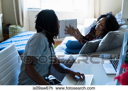 Stock Image - Lesbian couple in bedroom, reading and using computer. Fotosearch