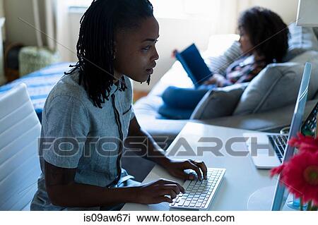 Stock Image - Lesbian couple in bedroom, reading and using computer. Fotosearch