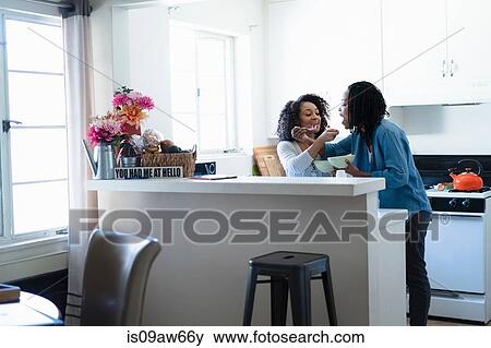 Stock Photo - Lesbian couple in kitchen, feeding each breakfast. Fotosearch