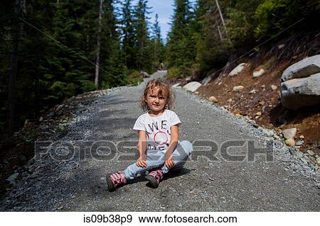 Stock Photo - Little girl sitting on gravel road in forest, Vancouver, British Columbia, Canada. Fotosearch