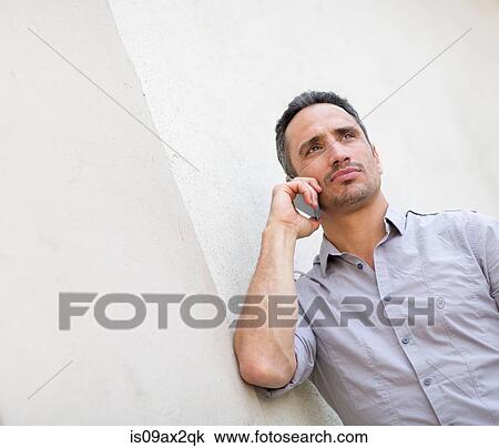 Low angle view of man leaning against wall making telephone call on smartphone View Large Photo Image Stock Image - Low angle view of man leaning against wall making telephone call on smartphone. Fotosearch
