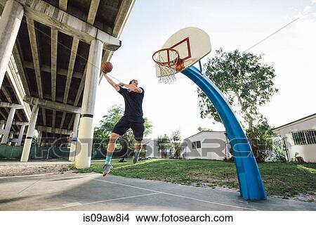 Picture - Low angle view of man on basketball court in mid air jumping for basketball hoop. Fotosearch