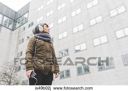 Low angle view of mid adult woman listening to headphones looking at city office block View Large Photo Image Stock Image - Low angle view of mid adult woman listening to headphones looking at city office block. Fotosearch