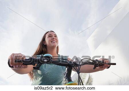 Stock Image - Low angle view of teenage girl cycling on bicycle. Fotosearch