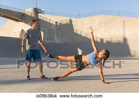 Stock Image - Male athlete helping friend with workout, Van Nuys, California, USA. Fotosearch