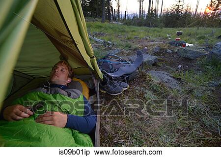 Stock Photography - Male camper in sleeping bag listening to earphones at dusk on Midnight Ridge, Colville National Forest, Washington State, USA. Fotosearch