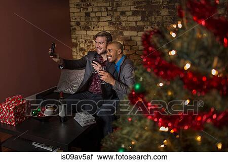 Male couple celebrating Christmas together, sitting on sofa, taking self portrait using smartphone View Large Photo Image Stock Image - Male couple celebrating Christmas together, sitting on sofa, taking self portrait using smartphone. Fotosearch