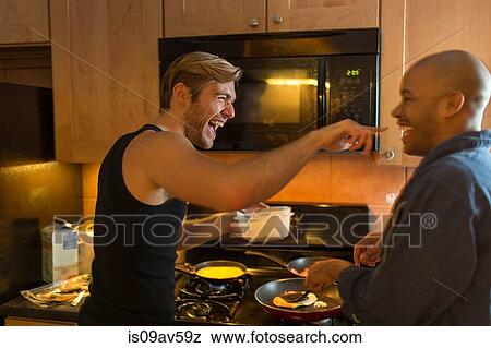 Stock Photo - Male couple in kitchen, fooling around, making breakfast. Fotosearch