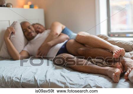 Stock Photograph - Male couple lying in bed together, hugging. Fotosearch