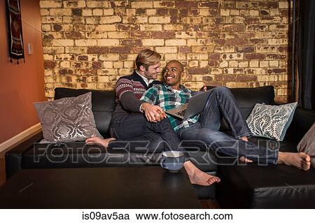 Male couple relaxing on sofa together, looking at laptop View Large Photo Image Stock Image - Male couple relaxing on sofa together, looking at laptop. Fotosearch