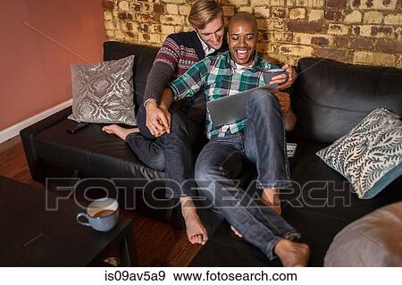 Male couple relaxing on sofa together, looking at laptop View Large Photo Image Stock Photo - Male couple relaxing on sofa together, looking at laptop. Fotosearch