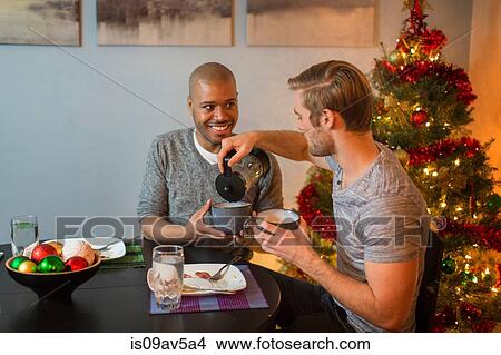 Male couple sitting at table, having breakfast together, Christmas tree in background View Large Photo Image Picture - Male couple sitting at table, having breakfast together, Christmas tree in background. Fotosearch