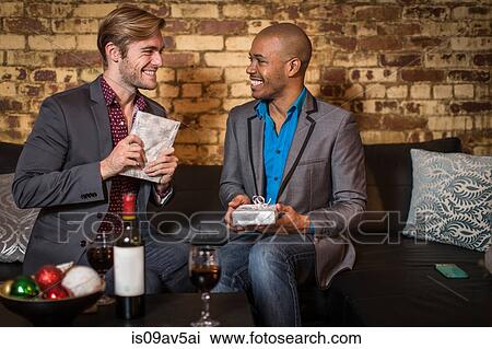 Male couple sitting on sofa, exchanging Christmas gifts View Large Photo Image Stock Image - Male couple sitting on sofa, exchanging Christmas gifts. Fotosearch
