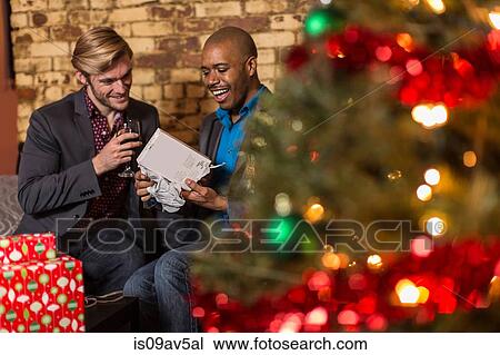 Male couple sitting on sofa, exchanging Christmas gifts View Large Photo Image Stock Image - Male couple sitting on sofa, exchanging Christmas gifts. Fotosearch