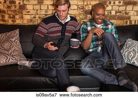 Male couple sitting on sofa, looking at smartphones View Large Photo Image Stock Photo - Male couple sitting on sofa, looking at smartphones. Fotosearch
