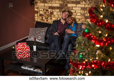 Male couple sitting on sofa, relaxing, at Christmas View Large Photo Image Picture - Male couple sitting on sofa, relaxing, at Christmas. Fotosearch