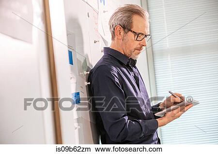 Picture - Male digital designer leaning against office wall making notes. Fotosearch