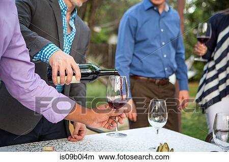 Picture - Male hands pouring red wine at garden party table. Fotosearch