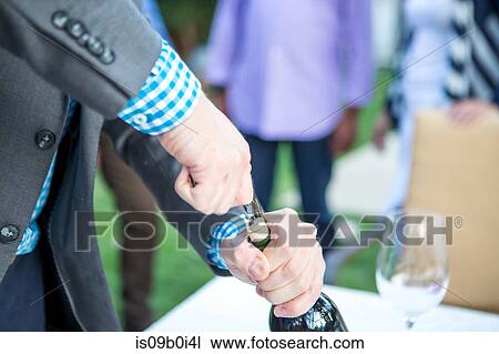 Stock Image - Male hands uncorking wine bottle at garden party table. Fotosearch