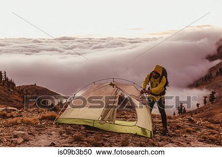 Stock Image - Male hiker putting up tent above the clouds, Mineral King, Sequoia National Park, California, USA. Fotosearch