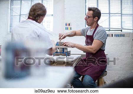 Stock Photograph - Male potter shaping clay pot on wheel in workshop. Fotosearch