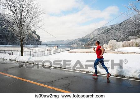 Stock Image - Male runner running along road in winter, Lake Kawaguchiko, Mount Fuji, Japan. Fotosearch