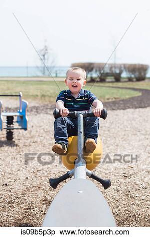 Stock Photography - Male toddler playing on seesaw in coastal park. Fotosearch