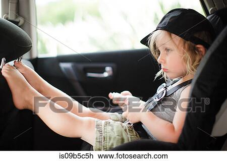 Stock Image - Male toddler with feet up staring in back seat of car. Fotosearch