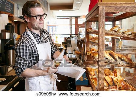 Male worker in bakery, putting baked goods into paper bag for customer View Large Photo Image Stock Photo - Male worker in bakery, putting baked goods into paper bag for customer. Fotosearch