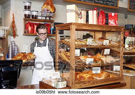 Stock Photograph - Male worker in bakery, putting fresh goods into display cabinet. Fotosearch