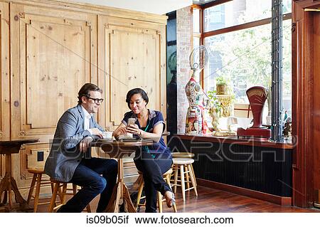 Man and woman sitting in cafe drinking coffee, looking at smartphone View Large Photo Image Stock Image - Man and woman sitting in cafe drinking coffee, looking at smartphone. Fotosearch