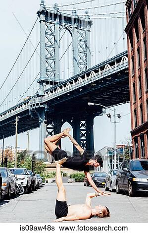 Man balancing on top of another in yoga position by Manhattan Bridge, New York, USA View Large Photo Image Stock Photograph - Man balancing on top of another in yoga position by Manhattan Bridge, New York, USA. Fotosearch