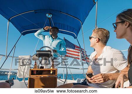 Man behind wheel of sailboat, enjoying view with friends View Large Photo Image Stock Photo - Man behind wheel of sailboat, enjoying view with friends. Fotosearch