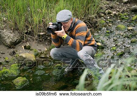 Man crouching in shallow river taking photograph View Large Photo Image Stock Photograph - Man crouching in shallow river taking photograph. Fotosearch