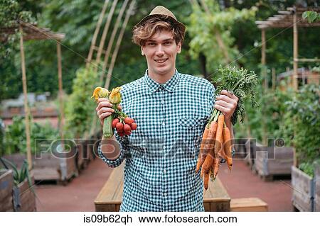 Stock Image - Man in garden holding bunches of carrots smiling. Fotosearch