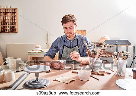 Stock Image - Man in workshop painting pottery. Fotosearch