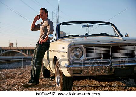 Stock Image - Man leaning against car making telephone call looking away, Los Angeles, California, USA. Fotosearch