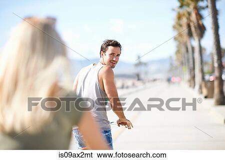 Man looking back at girlfriend whilst cycling at Venice Beach, Los Angeles, California, USA View Large Photo Image Stock Photograph - Man looking back at girlfriend whilst cycling at Venice Beach, Los Angeles, California, USA. Fotosearch