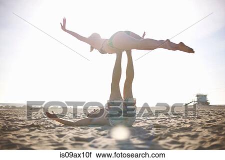 Stock Image - Man lying on beach balancing woman on feet. Fotosearch