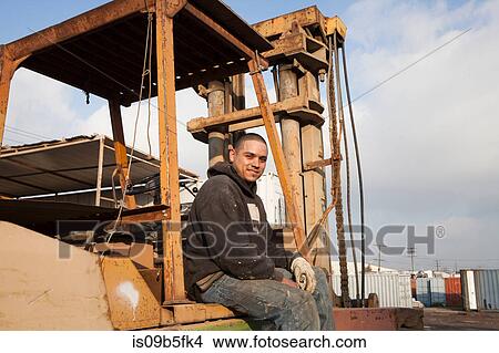 Man on construction site sitting on heavy machinery View Large Photo Image Picture - Man on construction site sitting on heavy machinery. Fotosearch
