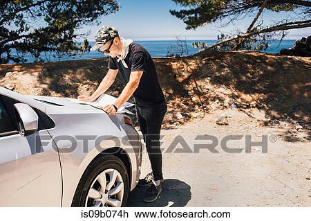 Stock Image - Man on road trip reading map on car hood, Big Sur, California, USA. Fotosearch