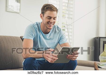 Man on sofa using digital tablet smiling View Large Photo Image Stock Photo - Man on sofa using digital tablet smiling. Fotosearch