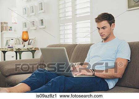 Stock Image - Man on sofa using laptop. Fotosearch