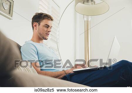 Stock Photography - Man on sofa using laptop. Fotosearch