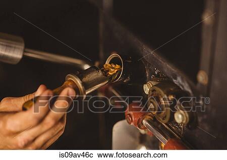 Stock Image - Man pouring coffee beans into coffee roaster, close-up. Fotosearch